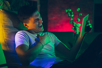 Image showing Cinematic portrait of handsome young man using devices, gadgets in neon lighted interior. Youth culture, bright colors