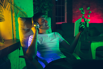 Image showing Cinematic portrait of handsome young man using devices, gadgets in neon lighted interior. Youth culture, bright colors