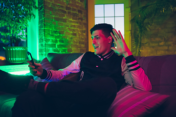 Image showing Cinematic portrait of handsome young man using devices, gadgets in neon lighted interior. Youth culture, bright colors