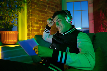 Image showing Cinematic portrait of handsome young man using devices, gadgets in neon lighted interior. Youth culture, bright colors