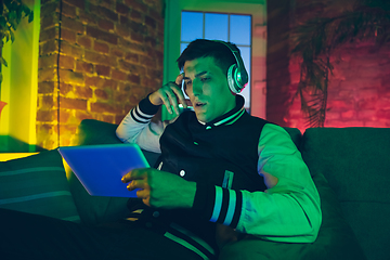 Image showing Cinematic portrait of handsome young man using devices, gadgets in neon lighted interior. Youth culture, bright colors