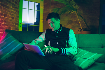 Image showing Cinematic portrait of handsome young man using devices, gadgets in neon lighted interior. Youth culture, bright colors