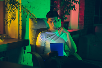 Image showing Cinematic portrait of handsome young man using devices, gadgets in neon lighted interior. Youth culture, bright colors