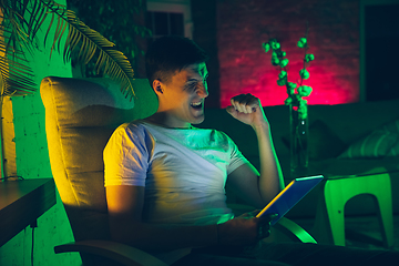 Image showing Cinematic portrait of handsome young man using devices, gadgets in neon lighted interior. Youth culture, bright colors