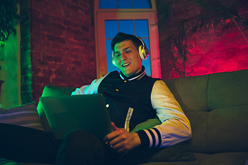 Image showing Cinematic portrait of handsome young man using devices, gadgets in neon lighted interior. Youth culture, bright colors