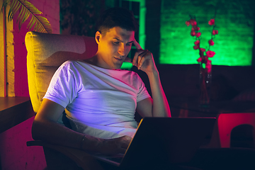 Image showing Cinematic portrait of handsome young man using devices, gadgets in neon lighted interior. Youth culture, bright colors