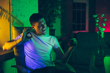 Image showing Cinematic portrait of handsome young man using devices, gadgets in neon lighted interior. Youth culture, bright colors