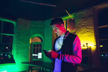 Image showing Cinematic portrait of handsome young man using devices, gadgets in neon lighted interior. Youth culture, bright colors