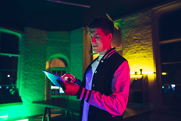 Image showing Cinematic portrait of handsome young man using devices, gadgets in neon lighted interior. Youth culture, bright colors