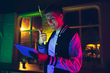 Image showing Cinematic portrait of handsome young man using devices, gadgets in neon lighted interior. Youth culture, bright colors