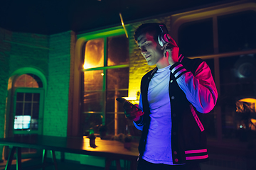 Image showing Cinematic portrait of handsome young man using devices, gadgets in neon lighted interior. Youth culture, bright colors