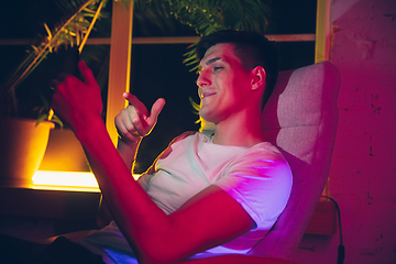 Image showing Cinematic portrait of handsome young man using devices, gadgets in neon lighted interior. Youth culture, bright colors