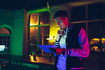 Image showing Cinematic portrait of handsome young man using devices, gadgets in neon lighted interior. Youth culture, bright colors