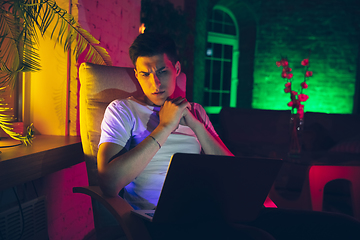 Image showing Cinematic portrait of handsome young man using devices, gadgets in neon lighted interior. Youth culture, bright colors