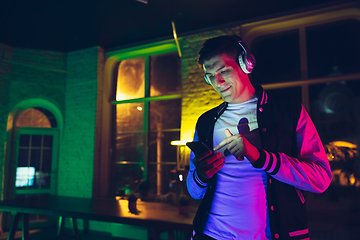 Image showing Cinematic portrait of handsome young man using devices, gadgets in neon lighted interior. Youth culture, bright colors