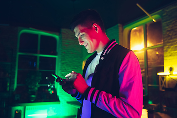 Image showing Cinematic portrait of handsome young man using devices, gadgets in neon lighted interior. Youth culture, bright colors