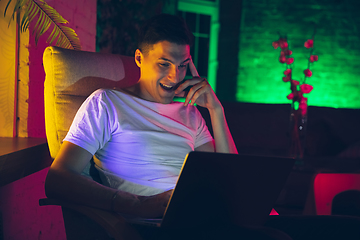 Image showing Cinematic portrait of handsome young man using devices, gadgets in neon lighted interior. Youth culture, bright colors