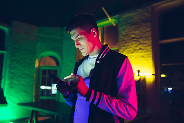 Image showing Cinematic portrait of handsome young man using devices, gadgets in neon lighted interior. Youth culture, bright colors