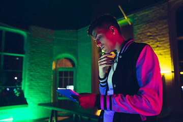 Image showing Cinematic portrait of handsome young man using devices, gadgets in neon lighted interior. Youth culture, bright colors