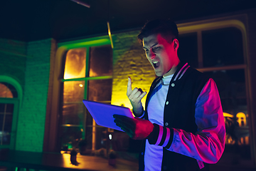 Image showing Cinematic portrait of handsome young man using devices, gadgets in neon lighted interior. Youth culture, bright colors