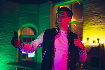 Image showing Cinematic portrait of handsome young man using devices, gadgets in neon lighted interior. Youth culture, bright colors