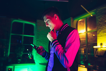 Image showing Cinematic portrait of handsome young man using devices, gadgets in neon lighted interior. Youth culture, bright colors