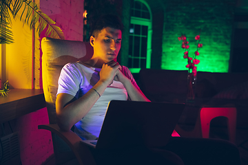 Image showing Cinematic portrait of handsome young man using devices, gadgets in neon lighted interior. Youth culture, bright colors