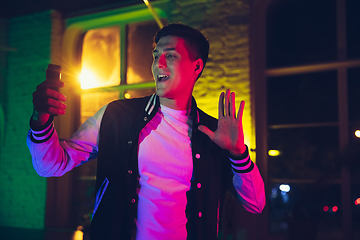 Image showing Cinematic portrait of handsome young man using devices, gadgets in neon lighted interior. Youth culture, bright colors