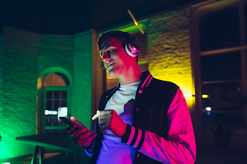 Image showing Cinematic portrait of handsome young man using devices, gadgets in neon lighted interior. Youth culture, bright colors