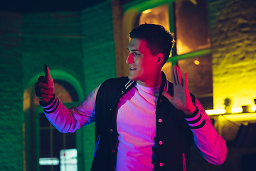 Image showing Cinematic portrait of handsome young man using devices, gadgets in neon lighted interior. Youth culture, bright colors