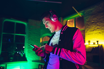 Image showing Cinematic portrait of handsome young man using devices, gadgets in neon lighted interior. Youth culture, bright colors