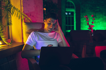 Image showing Cinematic portrait of handsome young man using devices, gadgets in neon lighted interior. Youth culture, bright colors