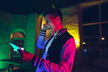 Image showing Cinematic portrait of handsome young man using devices, gadgets in neon lighted interior. Youth culture, bright colors