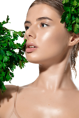 Image showing Vitamins. Close up of beautiful young woman with green leaves on her face over white background. Cosmetics and makeup, natural and eco treatment, skin care