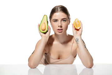 Image showing Choice. Beautiful young woman with fresh avocado and orange pieces over white background. Cosmetics and makeup, natural and eco treatment, skin care.