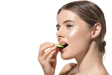 Image showing Nature way. Beautiful young woman biting fresh cucumber over white background. Cosmetics and makeup, natural and eco treatment, skin care.