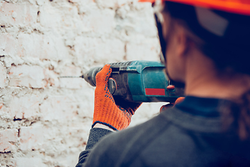 Image showing Close up of hands of repairman, professional builder working indoors, drills a wall