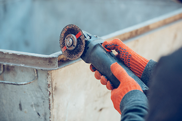 Image showing Close up of hands of repairman, professional builder working outdoors, cuts grinder