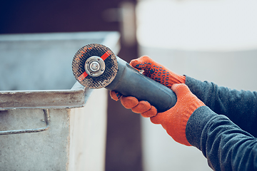 Image showing Close up of hands of repairman, professional builder working outdoors, cuts grinder