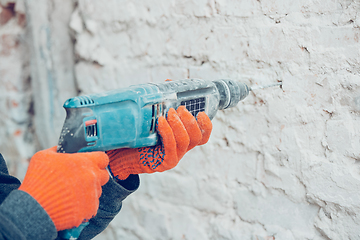 Image showing Close up of hands of repairman, professional builder working indoors, drills a wall