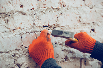 Image showing Close up of hands of repairman, professional builder working indoors, hammer a dowel with a screw into the wall