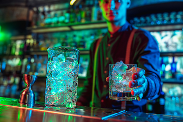 Image showing Close up of barman finishes preparation of alcoholic cocktail in multicolored neon light