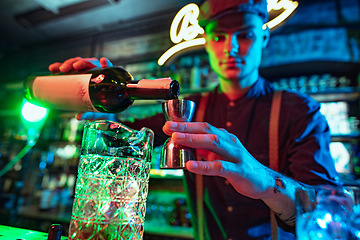 Image showing Barman finishes preparation of alcoholic cocktail with shot in multicolored neon light