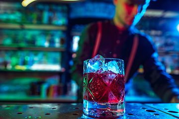 Image showing Close up of barman finishes preparation of alcoholic cocktail in multicolored neon light