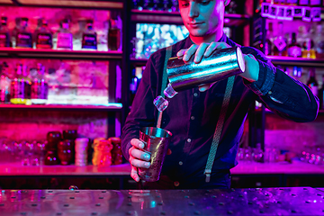 Image showing Close up of barman finishes preparation of alcoholic cocktail with shaker in multicolored neon light