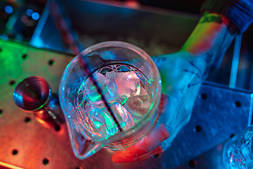 Image showing Top view of barman finishes preparation of alcoholic liquor and ice cocktail in multicolored neon light