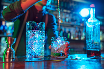 Image showing Close up of barman finishes preparation of alcoholic liquor and ice cocktail in multicolored neon light