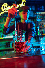 Image showing Close up of barman finishes preparation of alcoholic cocktail in multicolored neon light