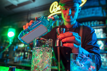 Image showing Barman finishes preparation of alcoholic cocktail with shot in multicolored neon light