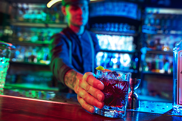 Image showing Close up of barman finishes preparation of alcoholic cocktail in multicolored neon light